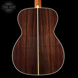 Back view of a wooden acoustic guitar with a visible brand logo in the corner.