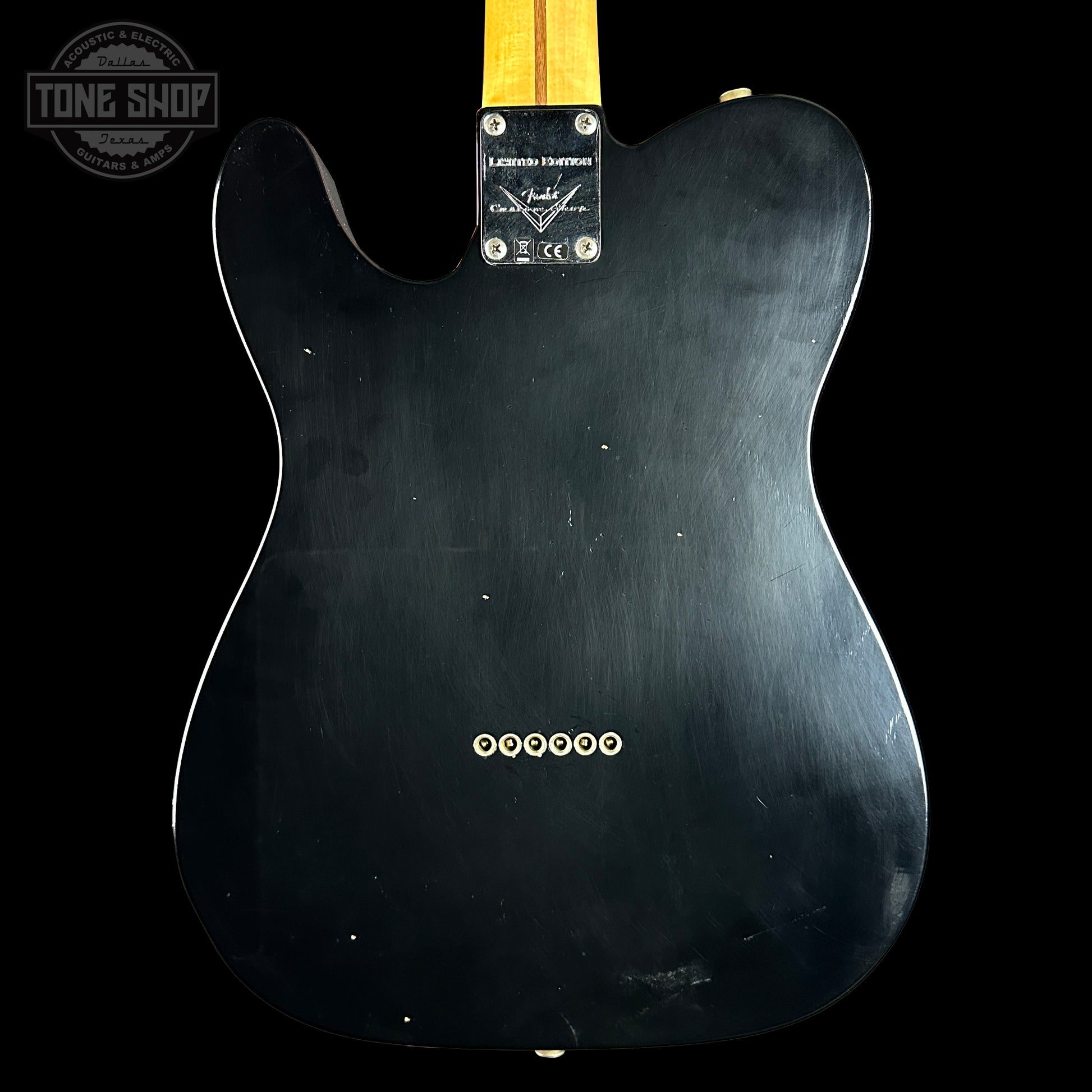 Back view of a black electric guitar with Fender logo on a black background