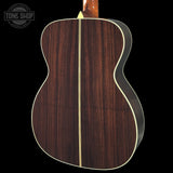 Back view of a wooden acoustic guitar with a visible brand logo in the corner.