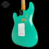 Turquoise electric guitar with a worn finish on a black background, featuring 'Tone Shop' branding.