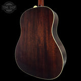 Back view of a wooden acoustic guitar with a dark brown finish on a black background.