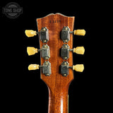 Close-up of a guitar headstock with tuning pegs on a black background, featuring the Tone Shop logo.