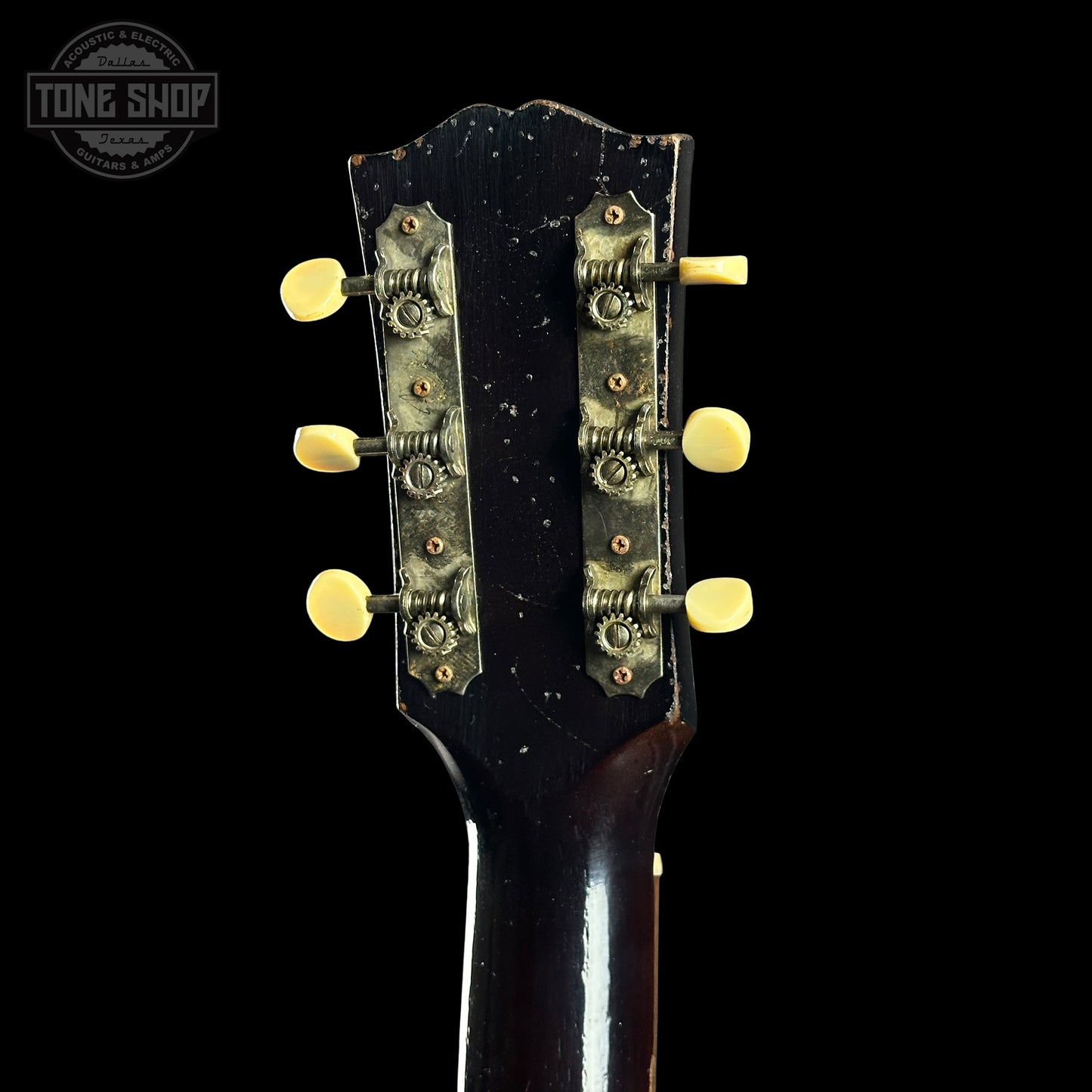 Close-up of a guitar headstock with tuning pegs on a black background, featuring 'Tone Shop' logo.