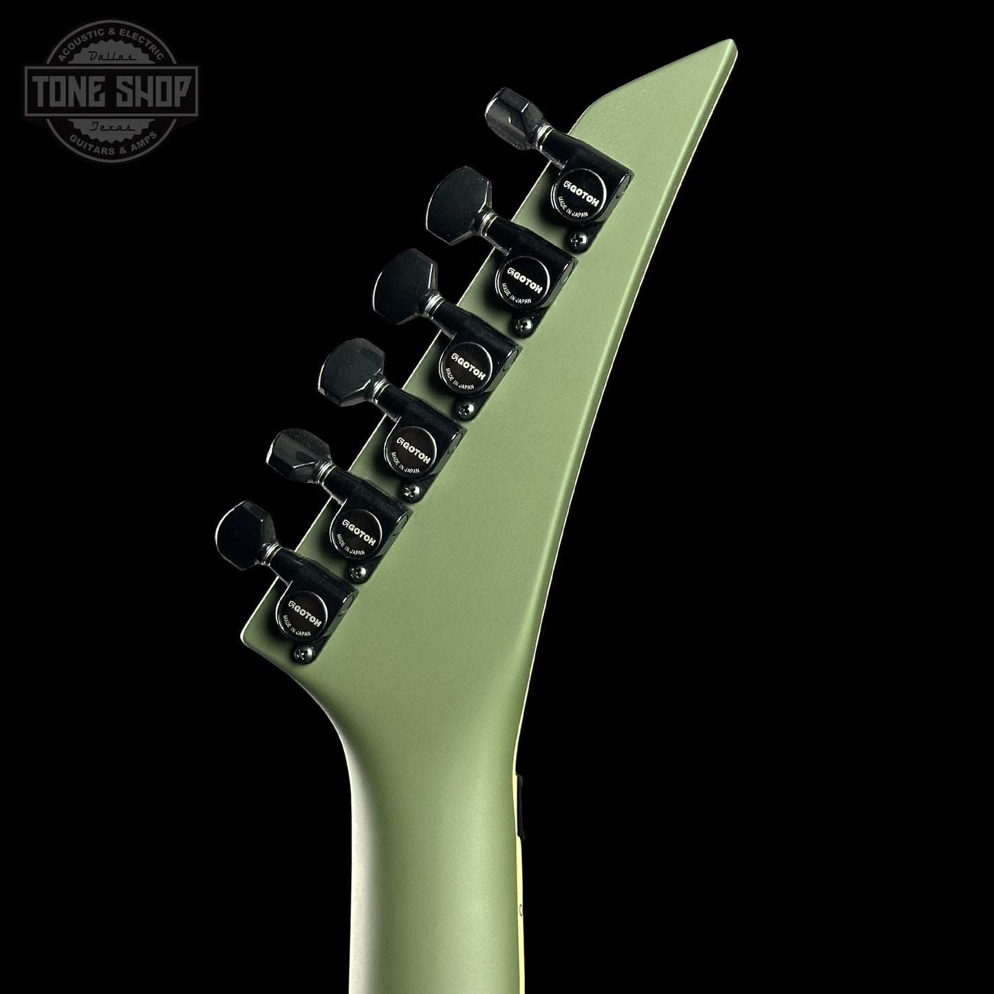 Close-up of a green electric guitar neck with a black Floyd Rose tremolo system on a black background.