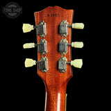 Close-up of a guitar headstock with tuning pegs on a black background, featuring the Tone Shop logo.