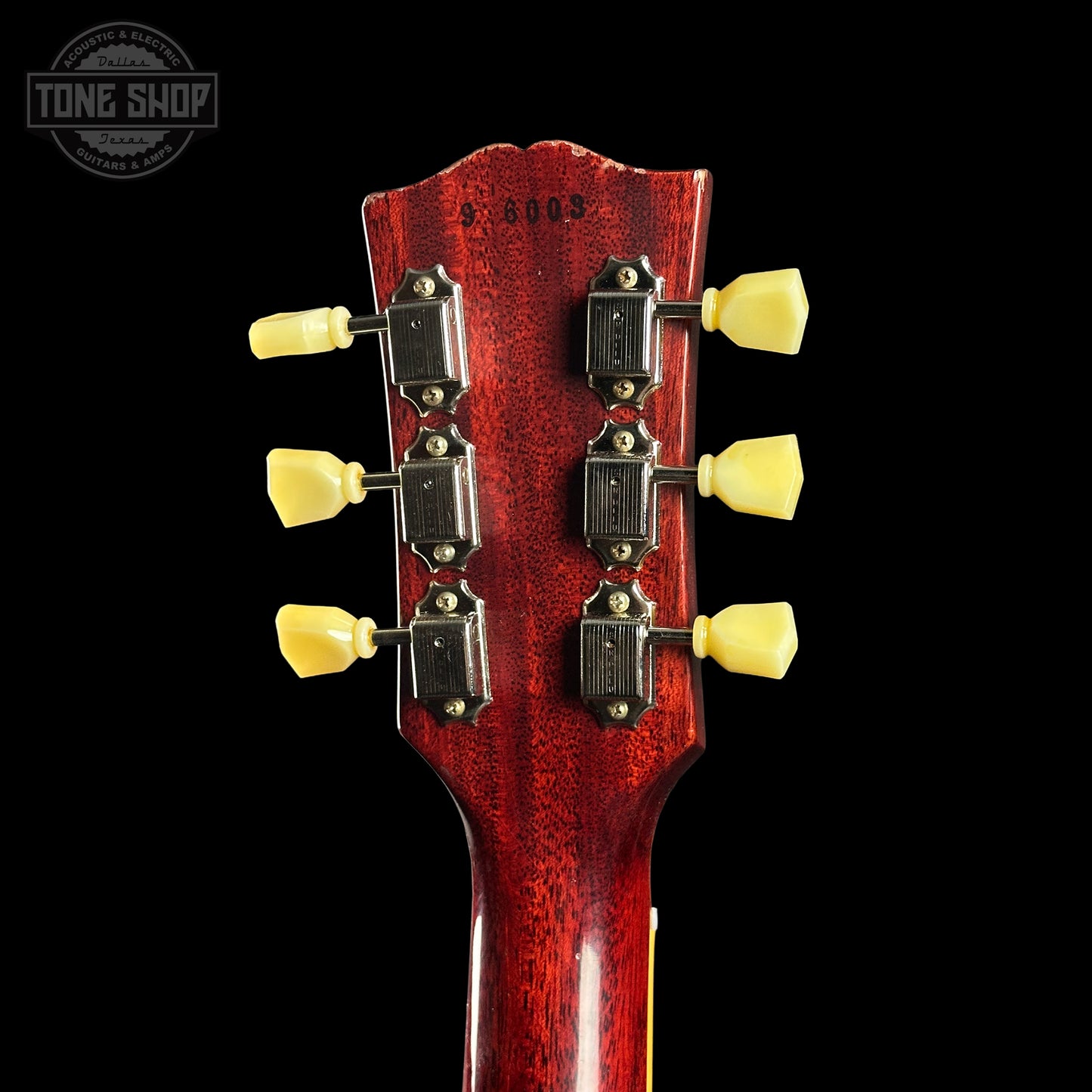 Close-up of a guitar headstock with tuning pegs on a black background, featuring the Tone Shop logo.