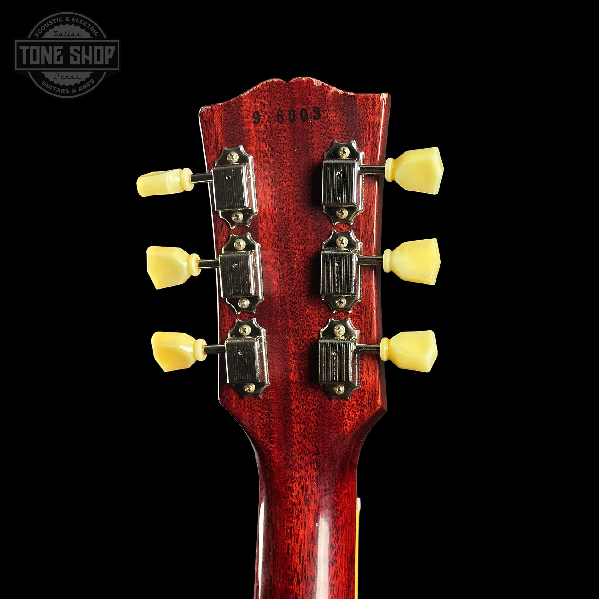 Close-up of a guitar headstock with tuning pegs on a black background, featuring the Tone Shop logo.