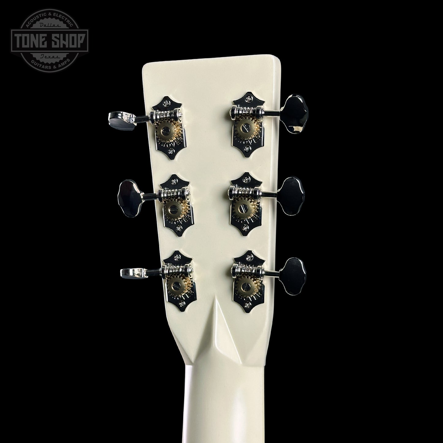 Close-up of a guitar headstock with tuning pegs on a black background, featuring the Tone Shop logo.
