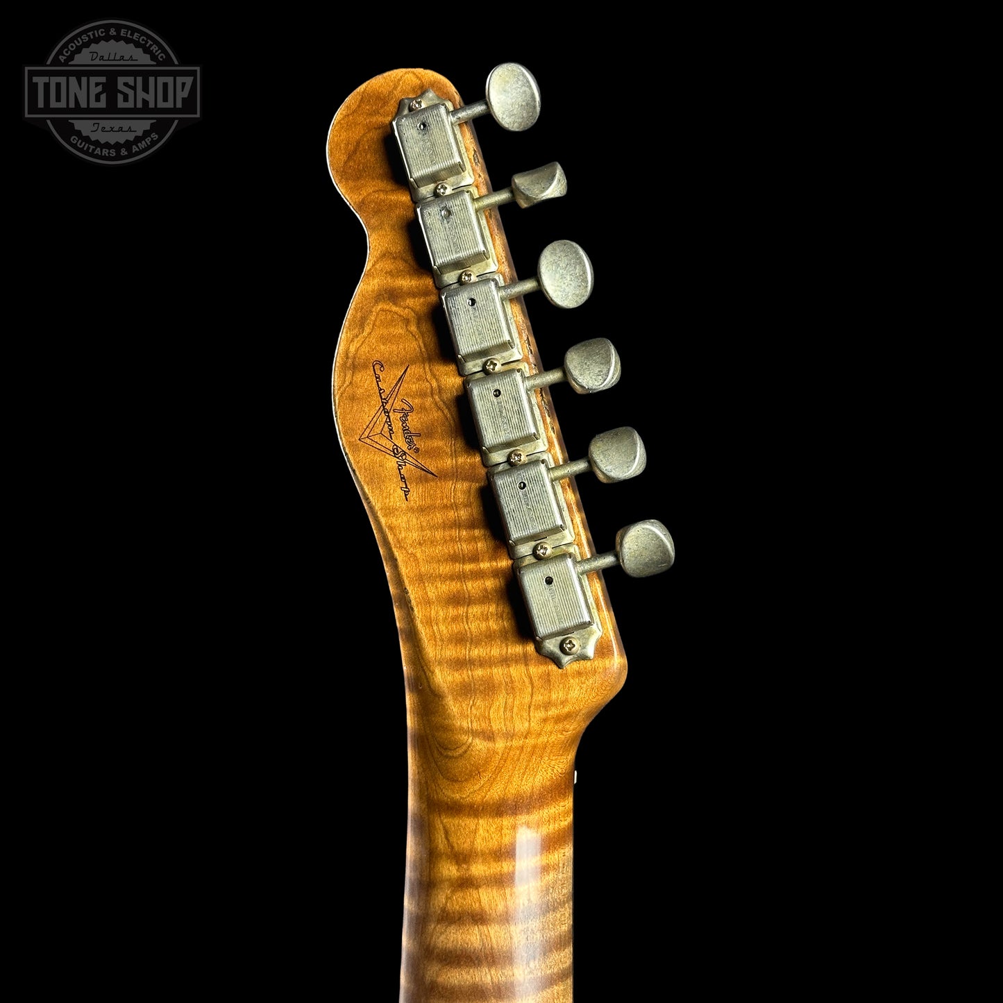 Close-up of a guitar neck with headstock and tuning pegs on a black background, featuring the Tone Shop logo.