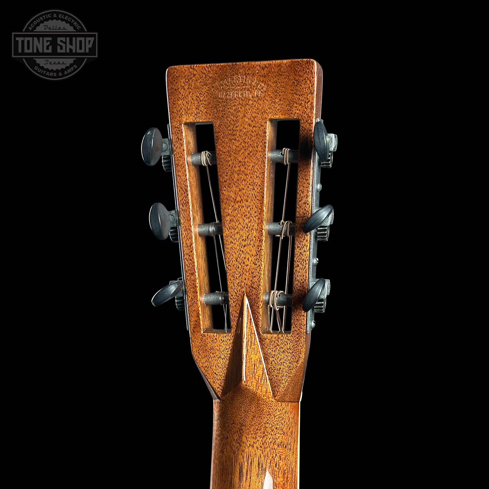 Close-up of a guitar headstock with tuning pegs on a black background, featuring the Tone Shop logo.