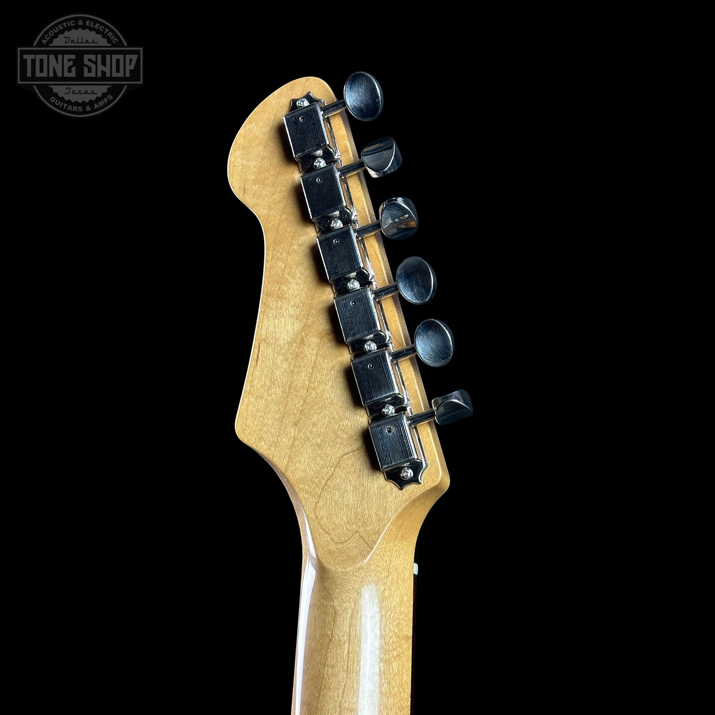Close-up of a guitar headstock with tuning pegs on a black background, featuring the Tone Shop logo.