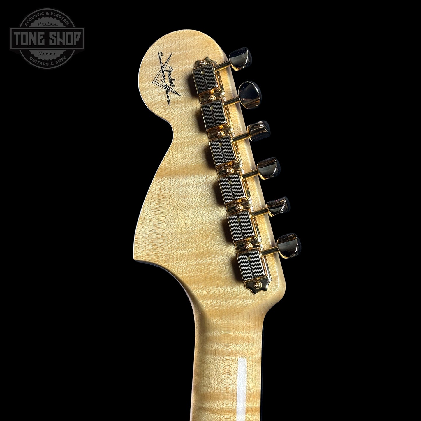 Close-up of a guitar headstock with tuning pegs on a black background, featuring the Tone Shop logo.