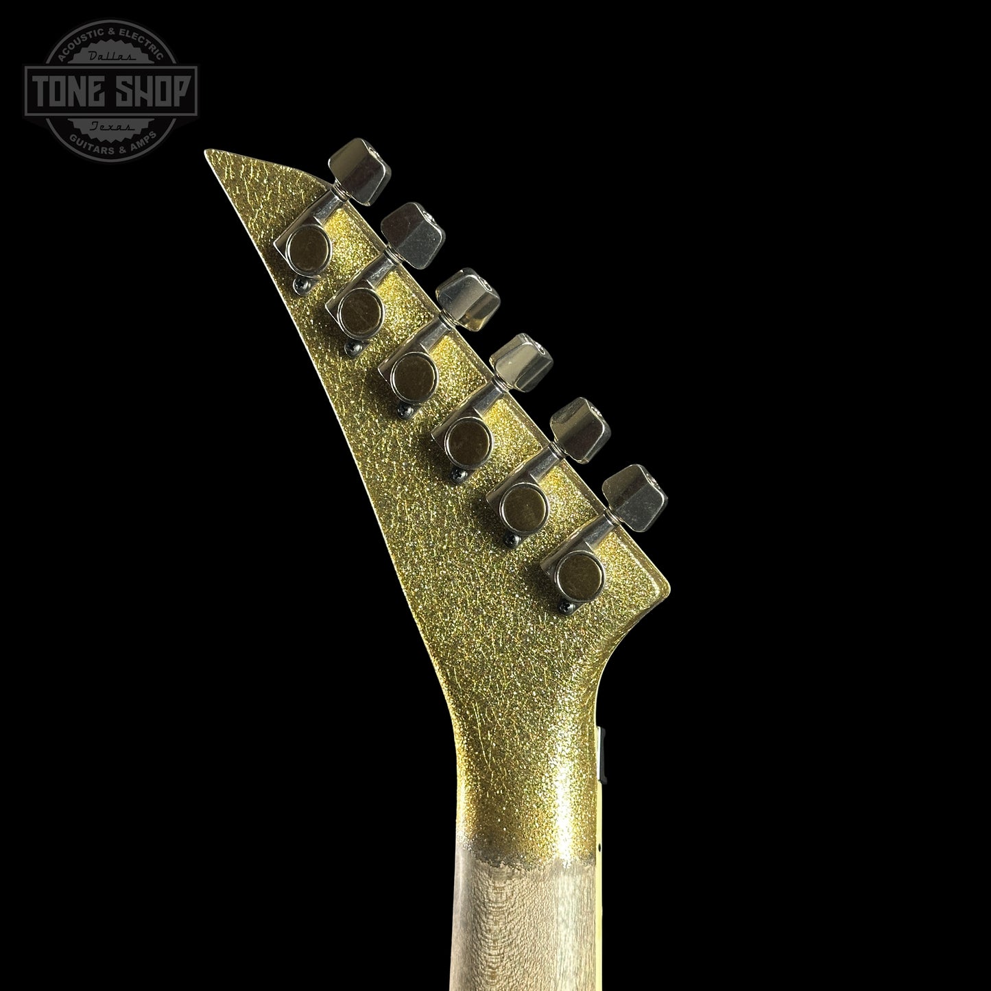 Close-up of a guitar neck with a metallic finish on a black background, featuring the Tone Shop logo.