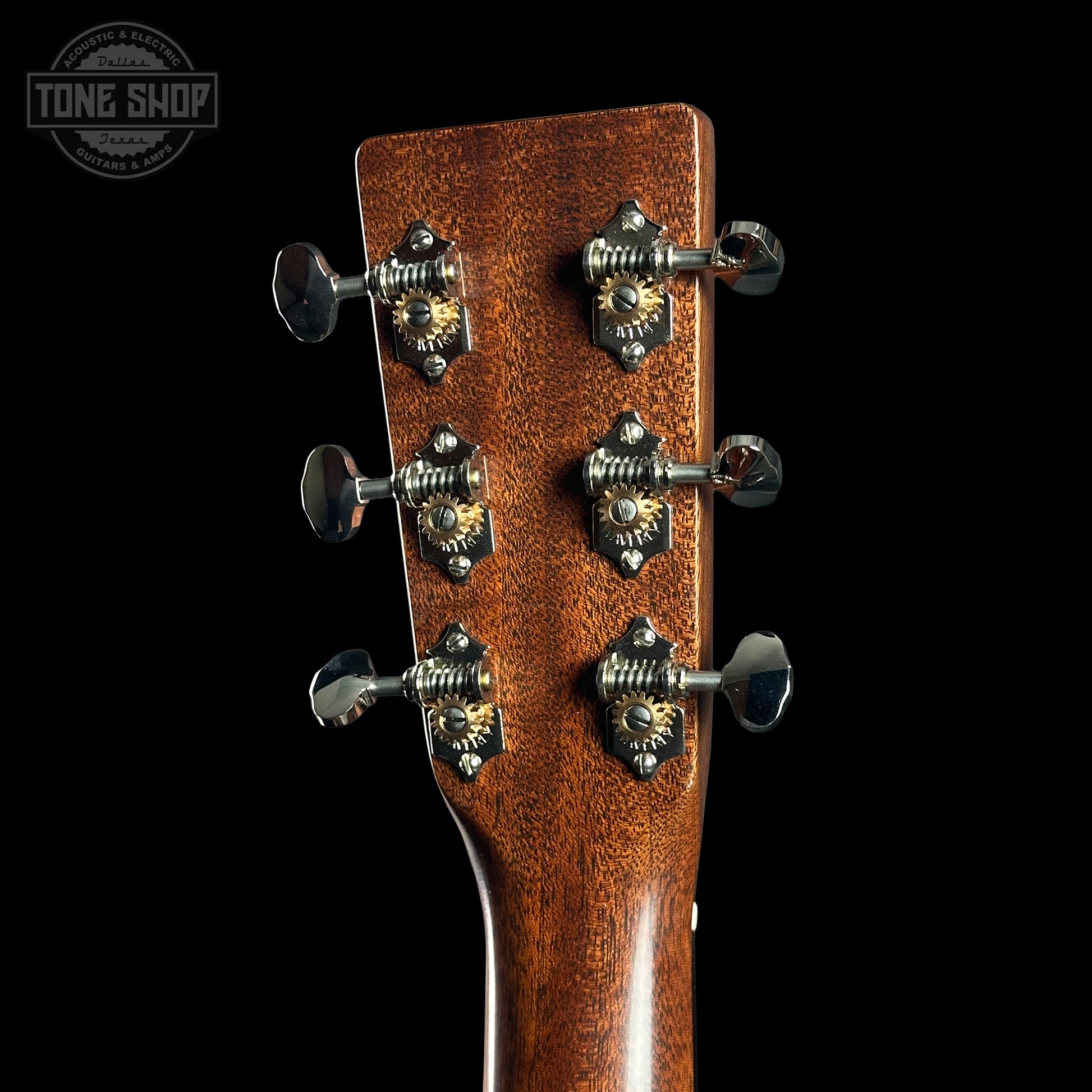 Close-up of a guitar headstock with tuning pegs on a black background, featuring the Tone Shop logo.