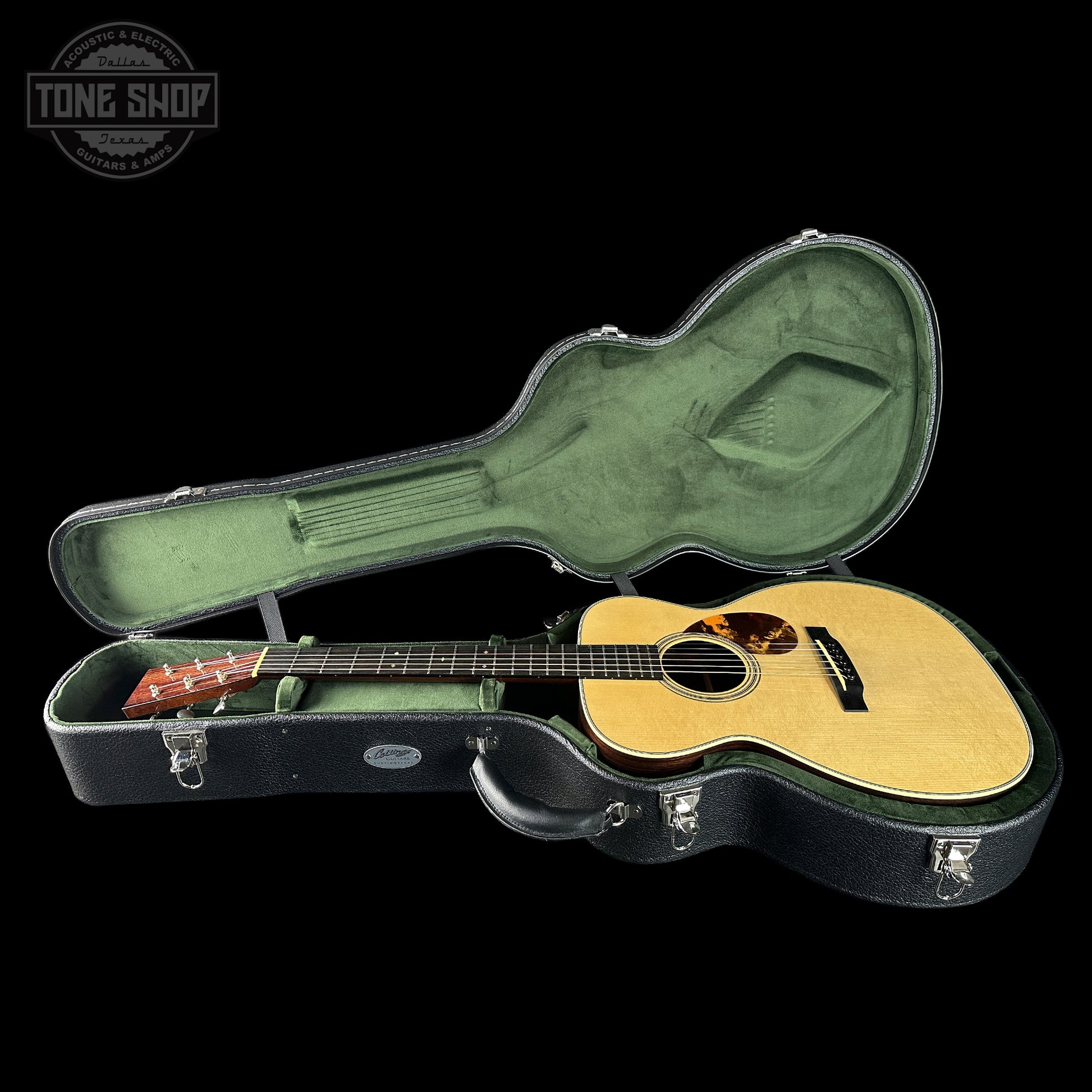 Acoustic guitar in a hard case with 'Tone Shop' logo in the corner.