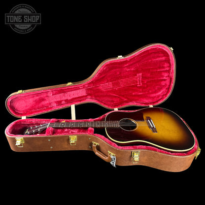 Acoustic guitar in a brown case with red interior on a black background, featuring 'Tone Shop' logo.