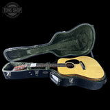 Acoustic guitar in a hard case with 'Tone Shop' logo in the corner.