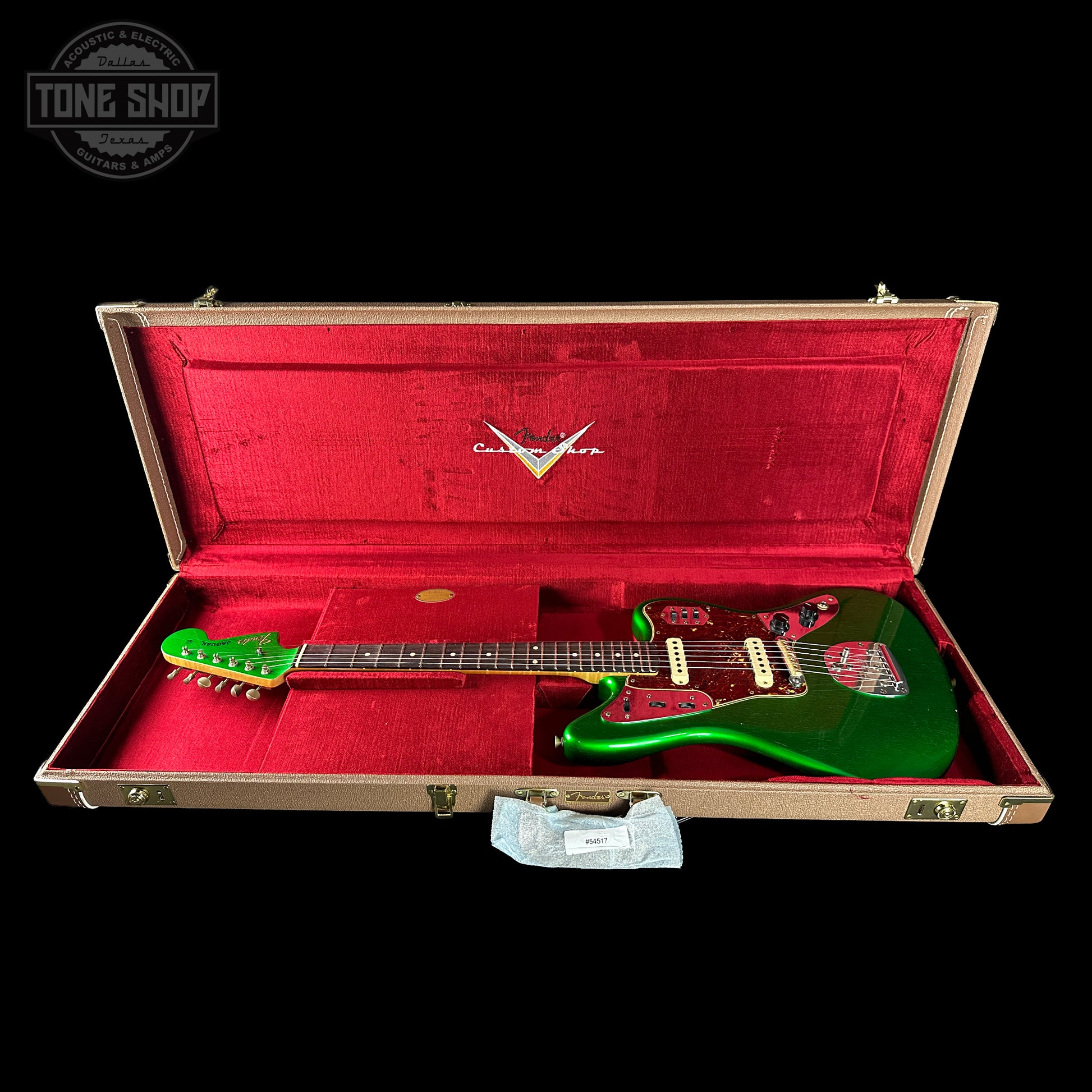 Green electric guitar in a red-lined case with a visible brand logo on a black background.