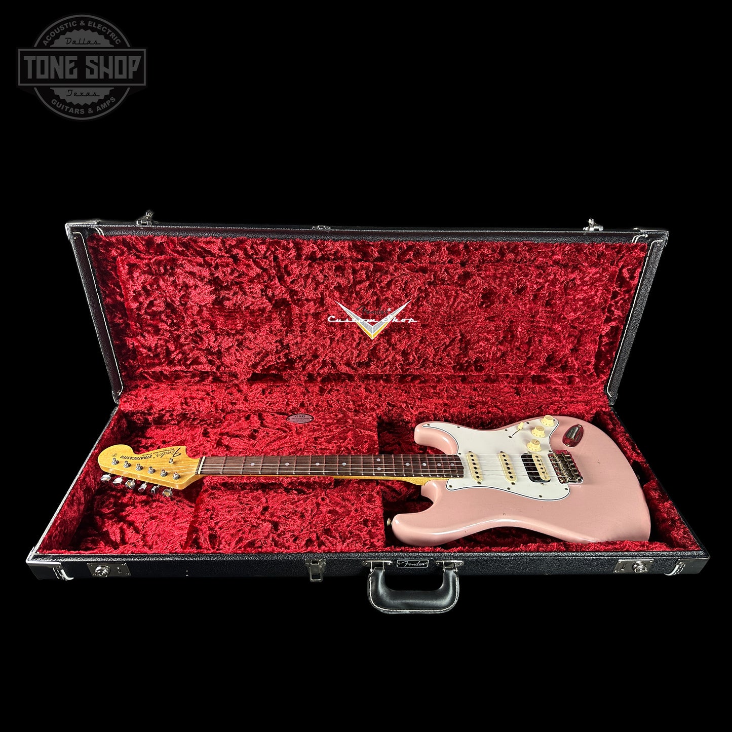 Pink electric guitar in a red-lined case with a 'Tone Shop' logo in the corner.