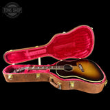 Acoustic guitar in a brown case with red interior on a black background, featuring 'Tone Shop' logo.