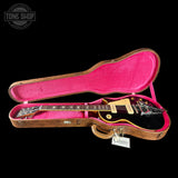 Electric guitar in a case with pink interior on a black background, featuring 'Tone Shop' logo.
