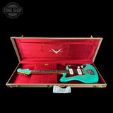 Turquoise electric guitar in a red-lined case with 'Tone Shop' logo.