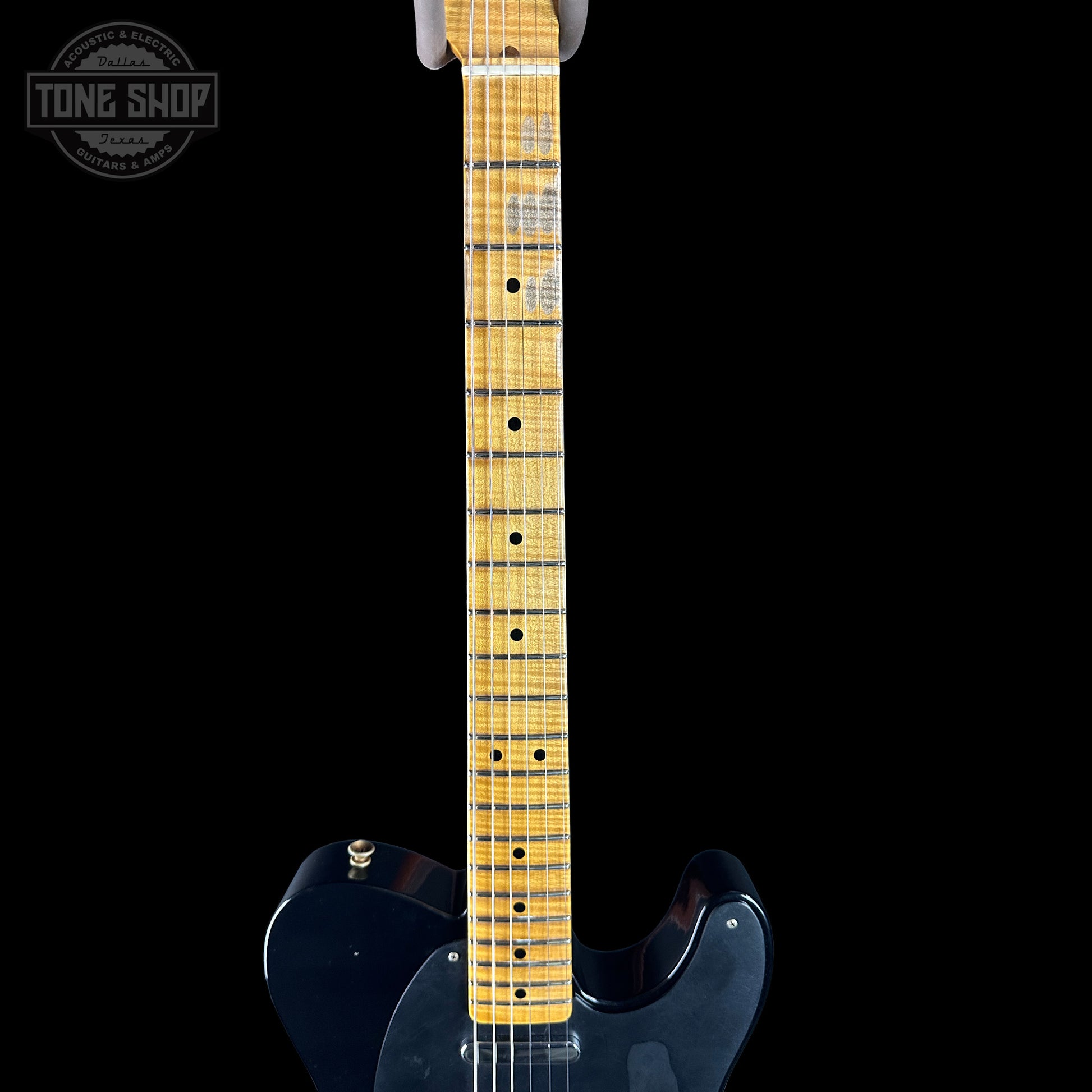 Close-up of a guitar neck with a black body on a black background, featuring the Tone Shop logo.