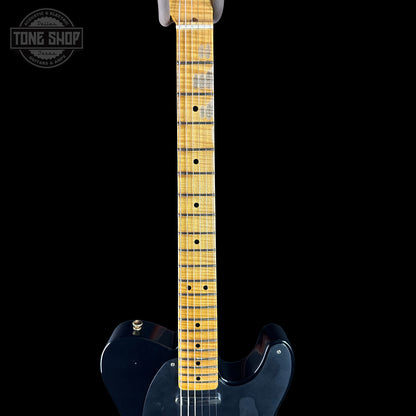 Close-up of a guitar neck with a black body on a black background, featuring the Tone Shop logo.