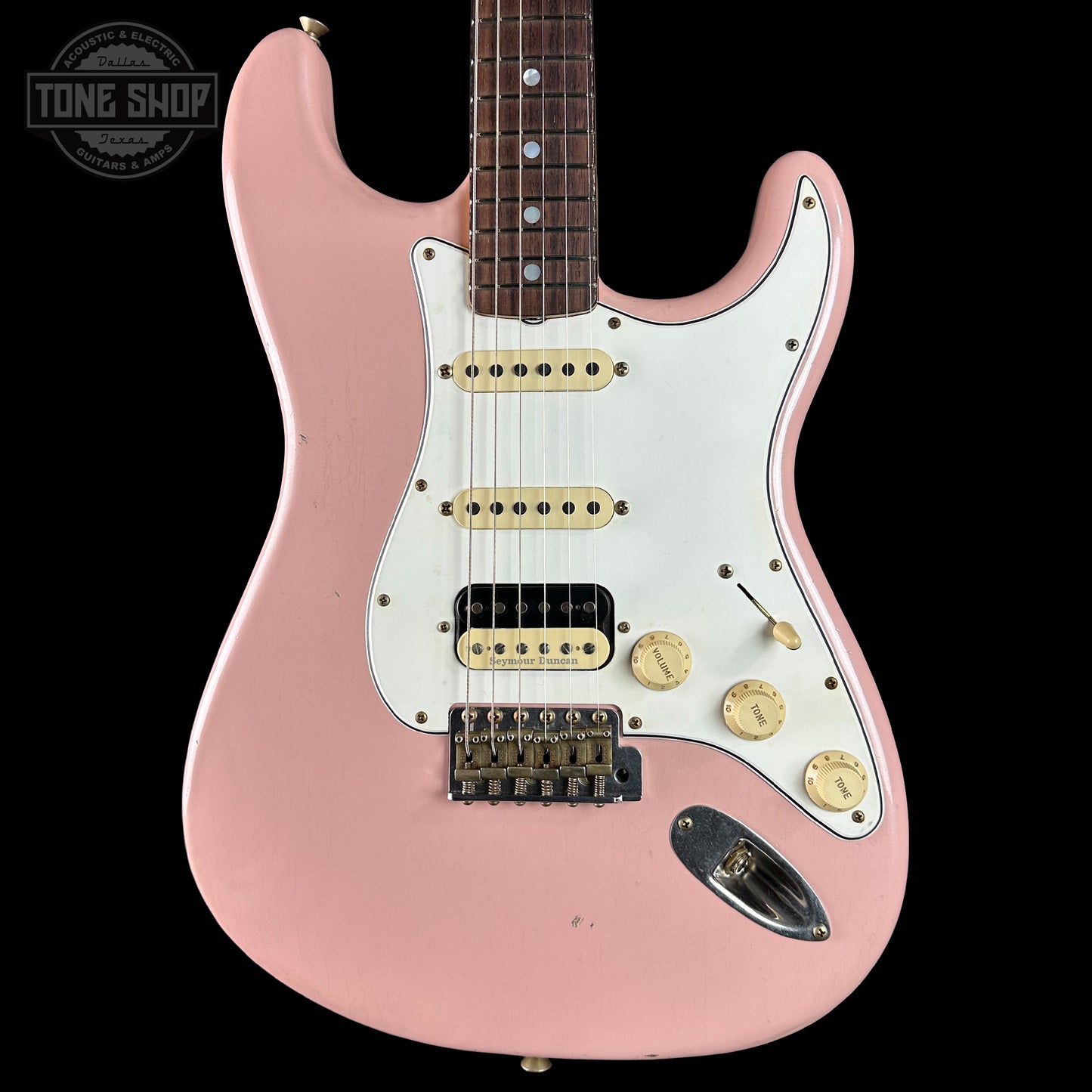 Pink electric guitar with a white pickguard on a black background, featuring the 'Tone Shop' logo.