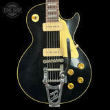 Black electric guitar with gold hardware on a black background, featuring the 'Tone Shop' logo.