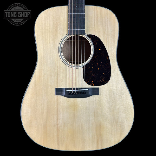 Acoustic guitar with a natural wood finish on a black background, featuring the Tone Shop logo.