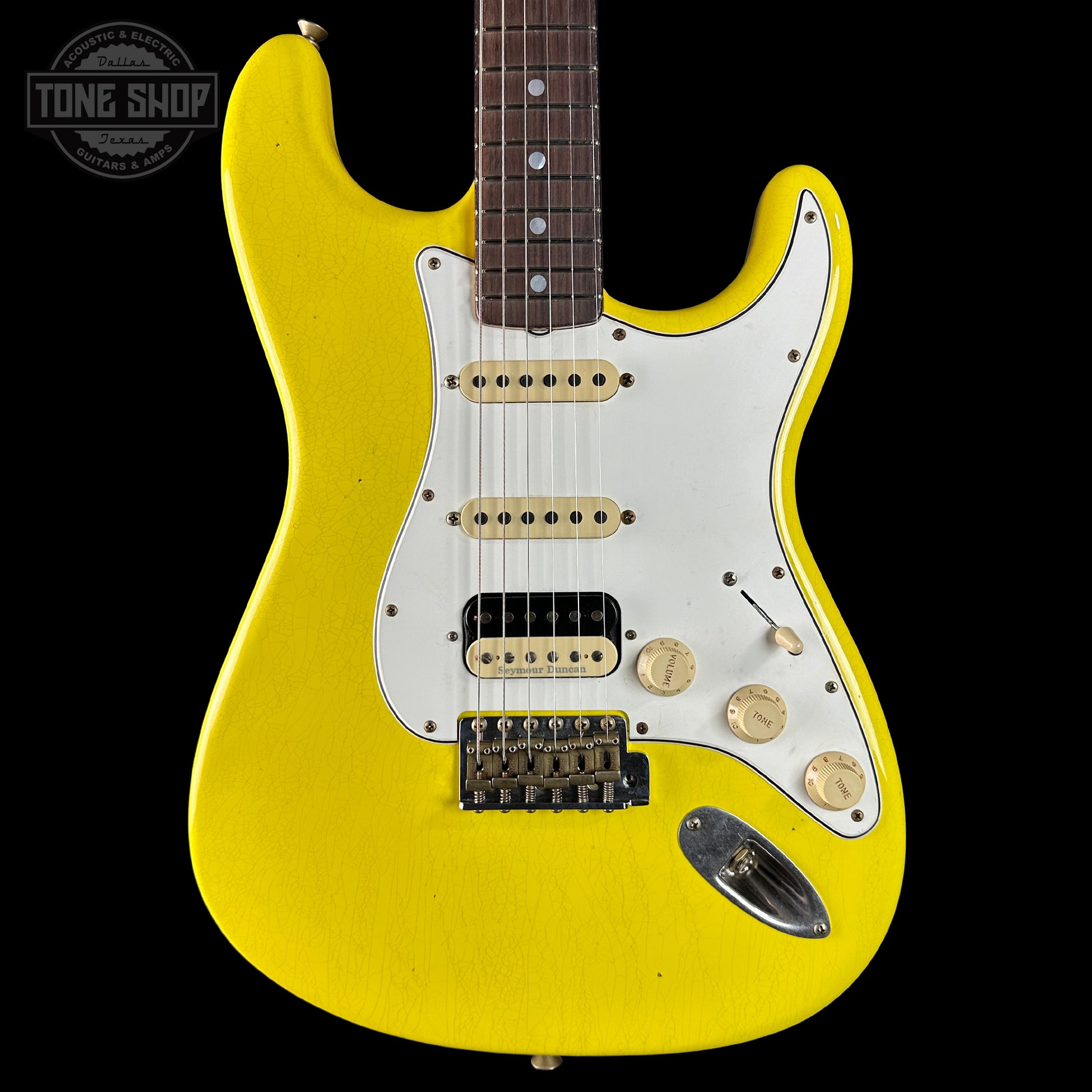 Yellow electric guitar with a white pickguard on a black background, featuring the Tone Shop logo.