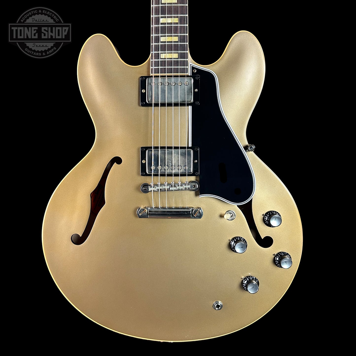 Gold electric guitar with a black pickguard on a black background, featuring 'Tone Shop' logo.