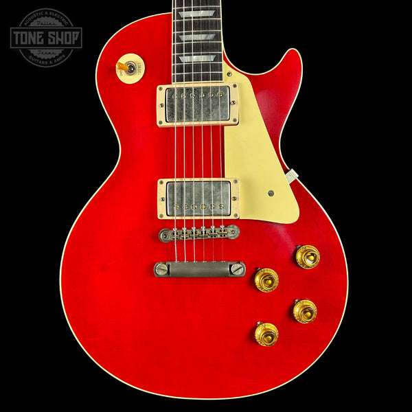 Red electric guitar with gold hardware on a black background, featuring 'Tone Shop' logo.