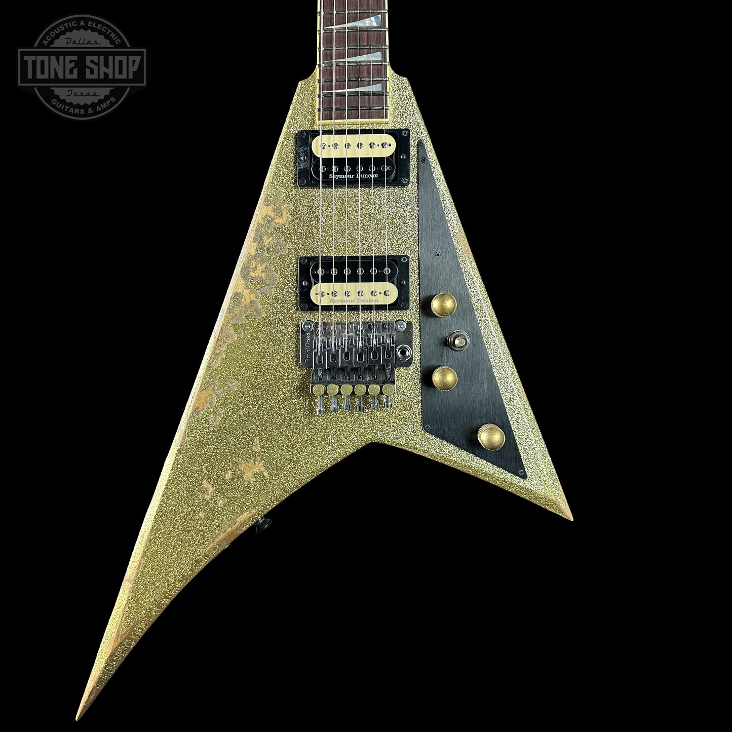 V-shaped electric guitar with a textured finish on a black background, featuring 'Tone Shop' branding.