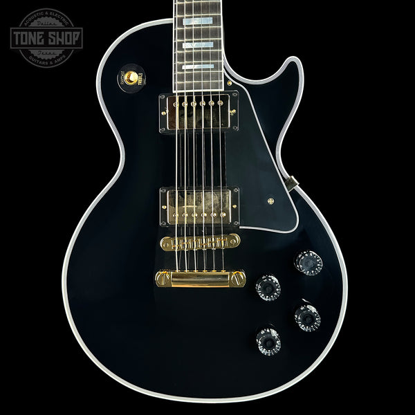 Black electric guitar with gold hardware on a black background, featuring 'Tone Shop' logo.