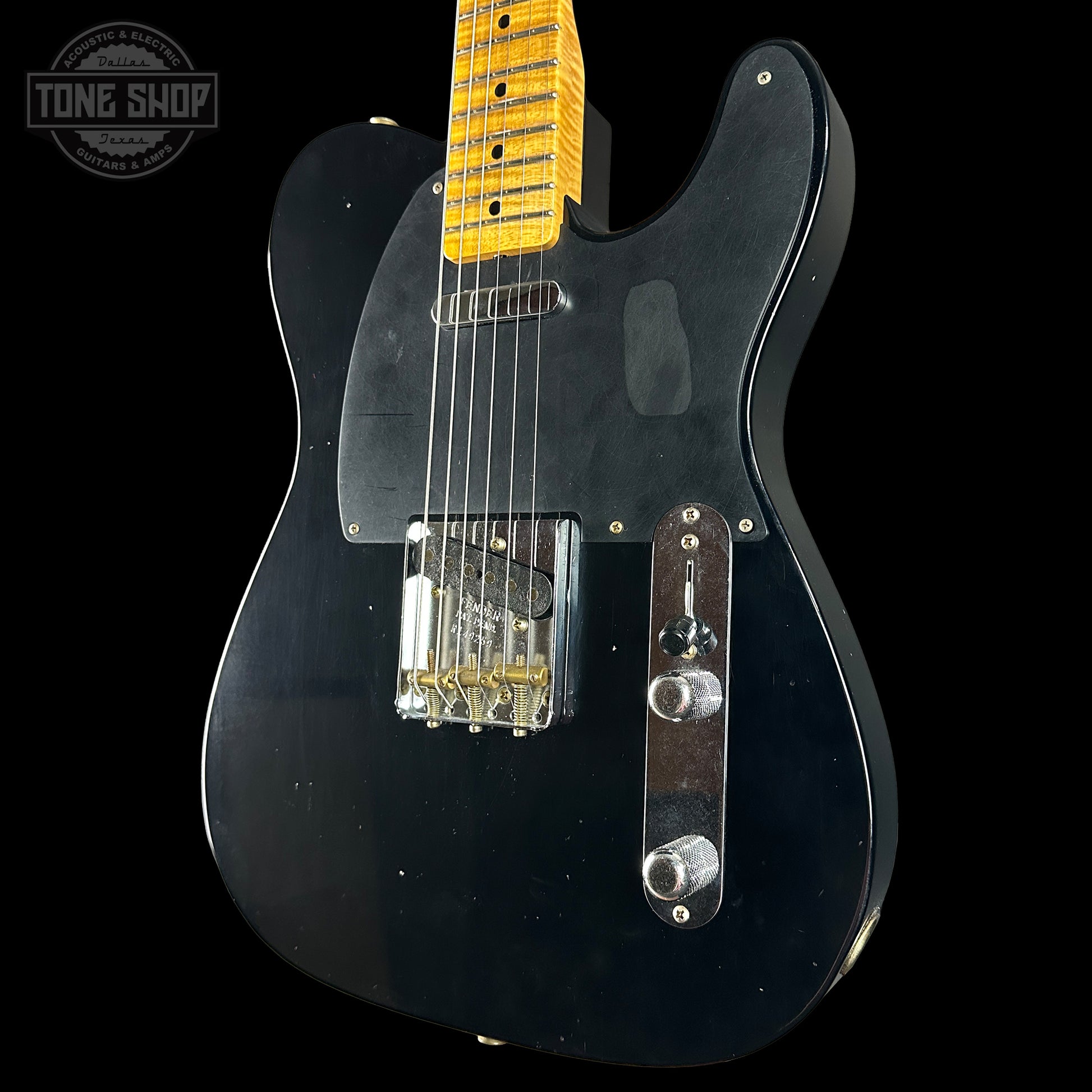 Black electric guitar with a yellow pickguard on a black background, featuring the Tone Shop logo.