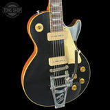 Black electric guitar with gold hardware on a black background, featuring 'Tone Shop' logo.