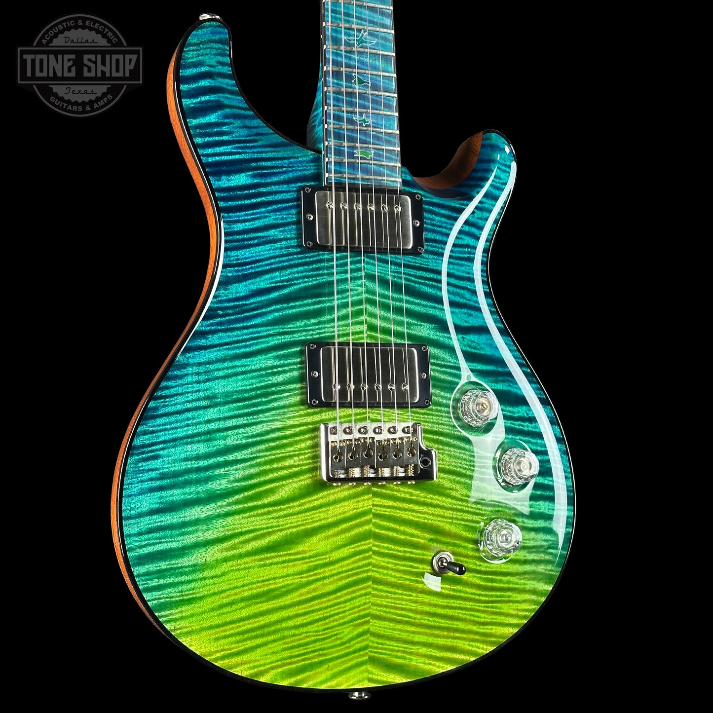 Electric guitar with a green and blue striped body on a black background, featuring the Tone Shop logo.