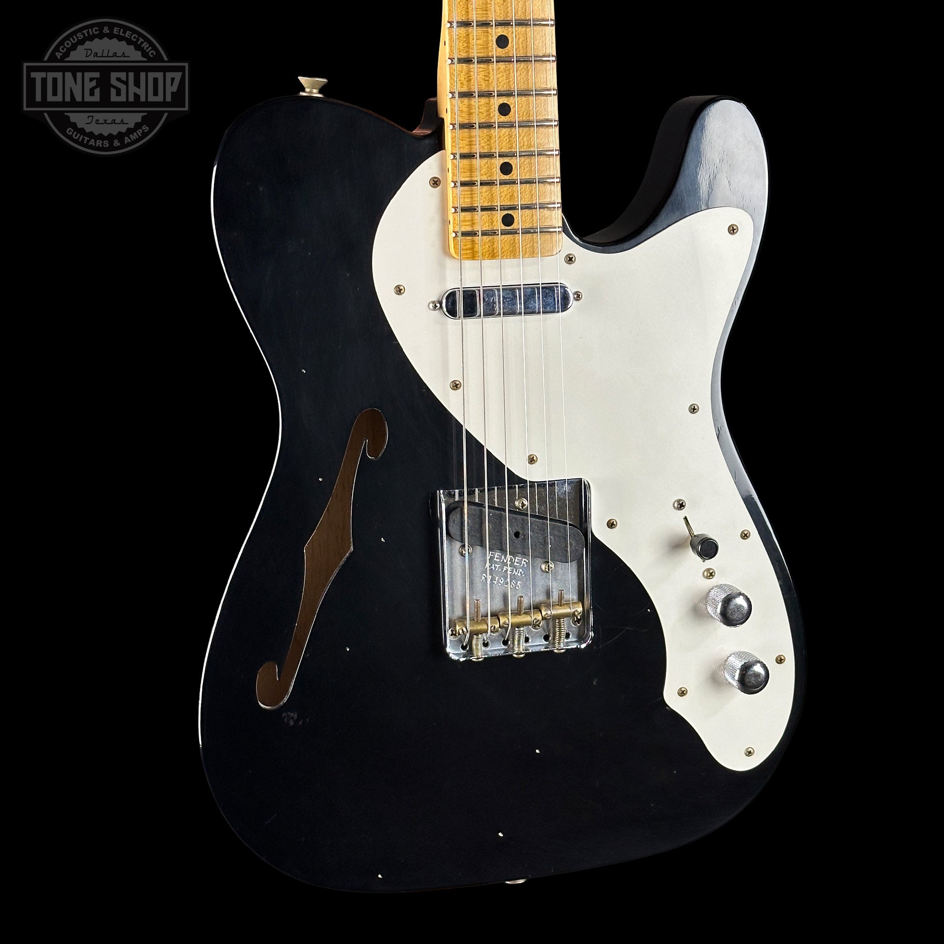 Black electric guitar with white pickguard on a black background, featuring 'Tone Shop' logo.