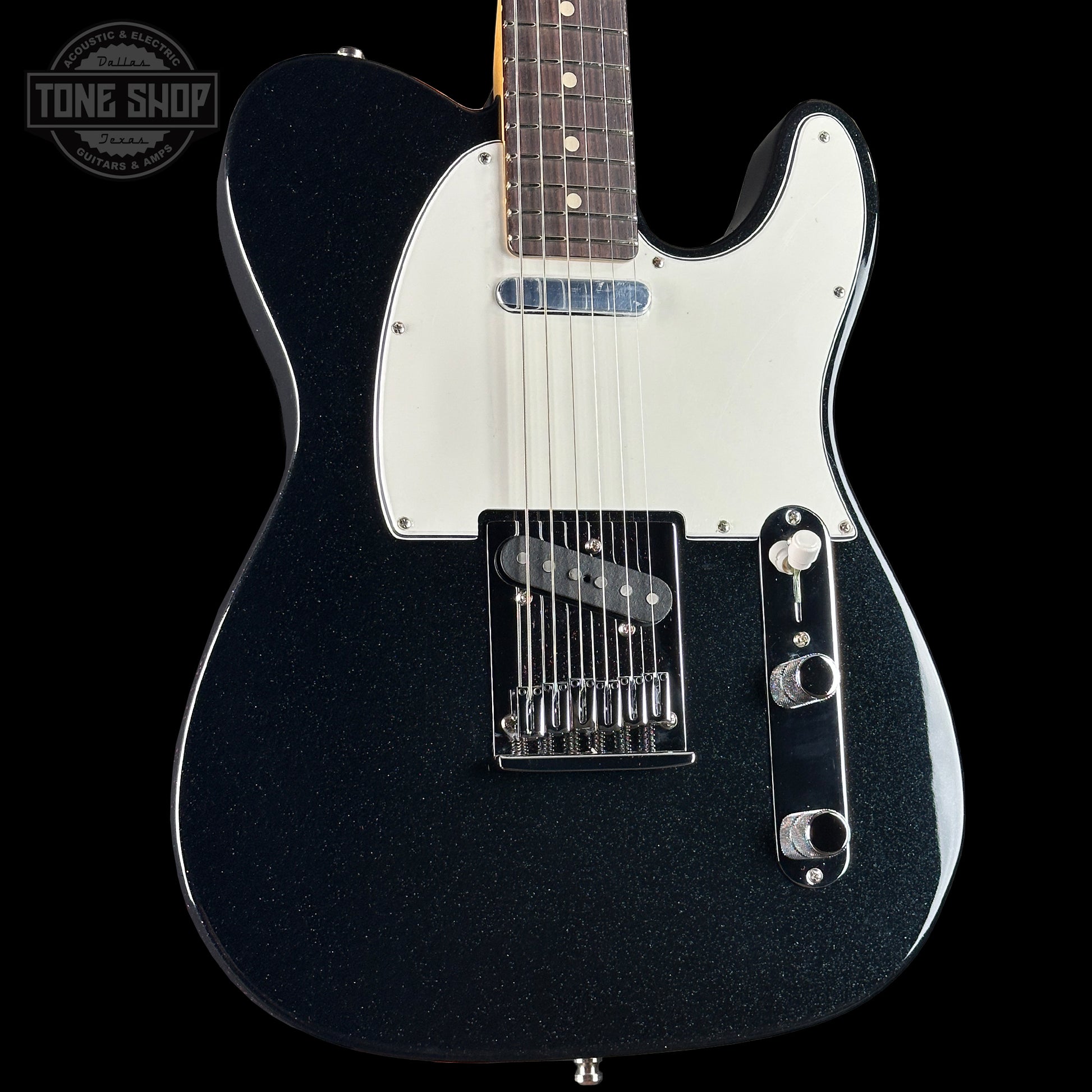 Black electric guitar with a white pickguard on a black background, featuring the Tone Shop logo.