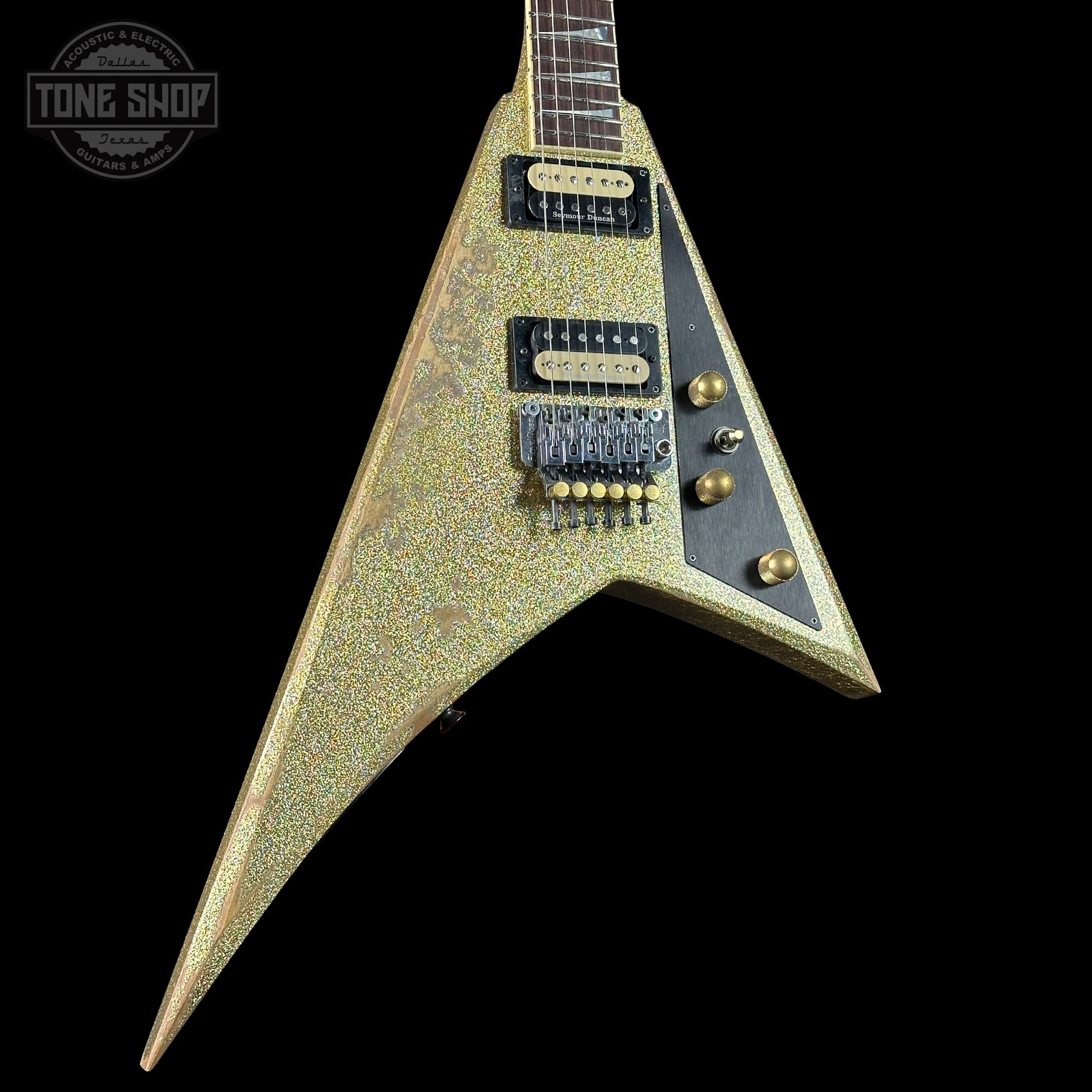 V-shaped electric guitar with a textured finish on a black background, featuring the Tone Shop logo.