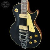 Black electric guitar with gold hardware on a black background, featuring 'Tone Shop' logo.