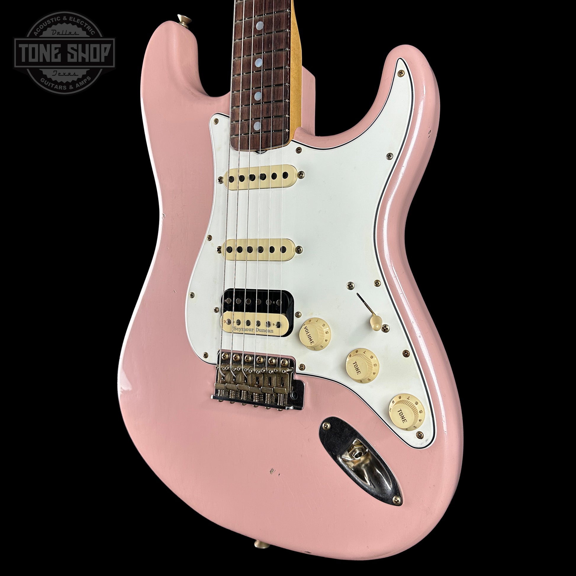 Pink electric guitar with a white pickguard on a black background, featuring the Tone Shop logo.