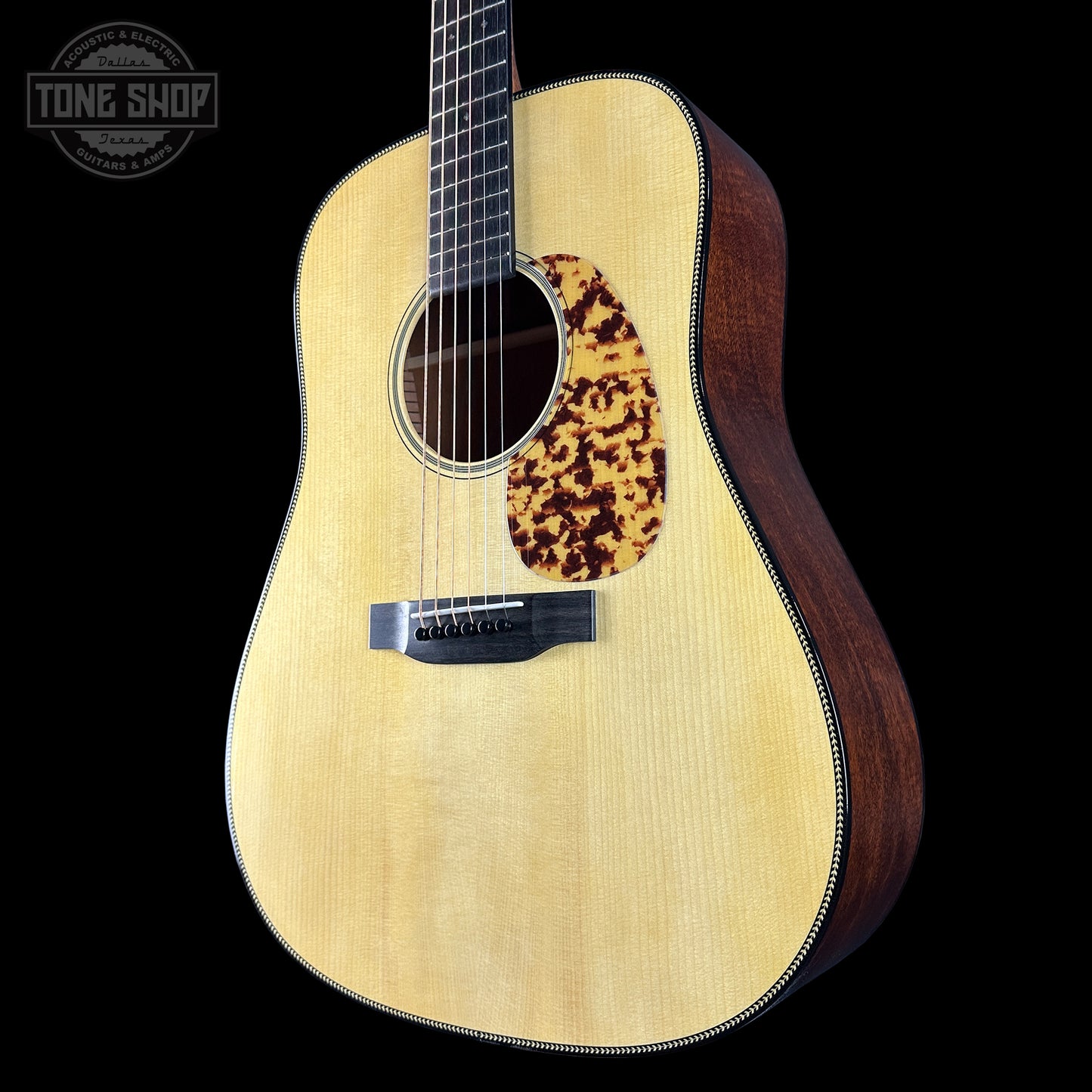 Acoustic guitar with a tortoiseshell pickguard on a black background, featuring the Tone Shop logo.