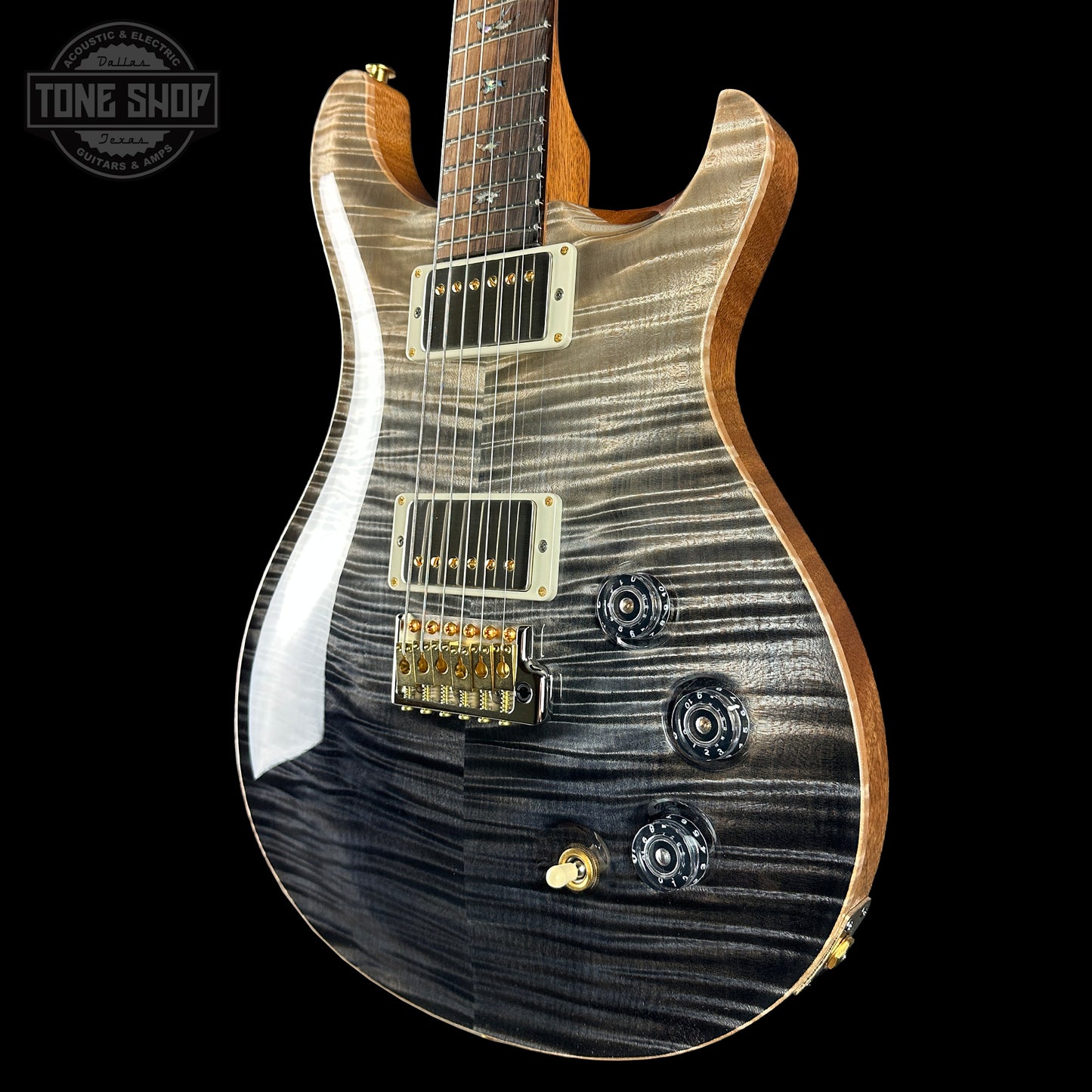 Close-up of a guitar with a black and brown pattern on a black background, featuring the Tone Shop logo.