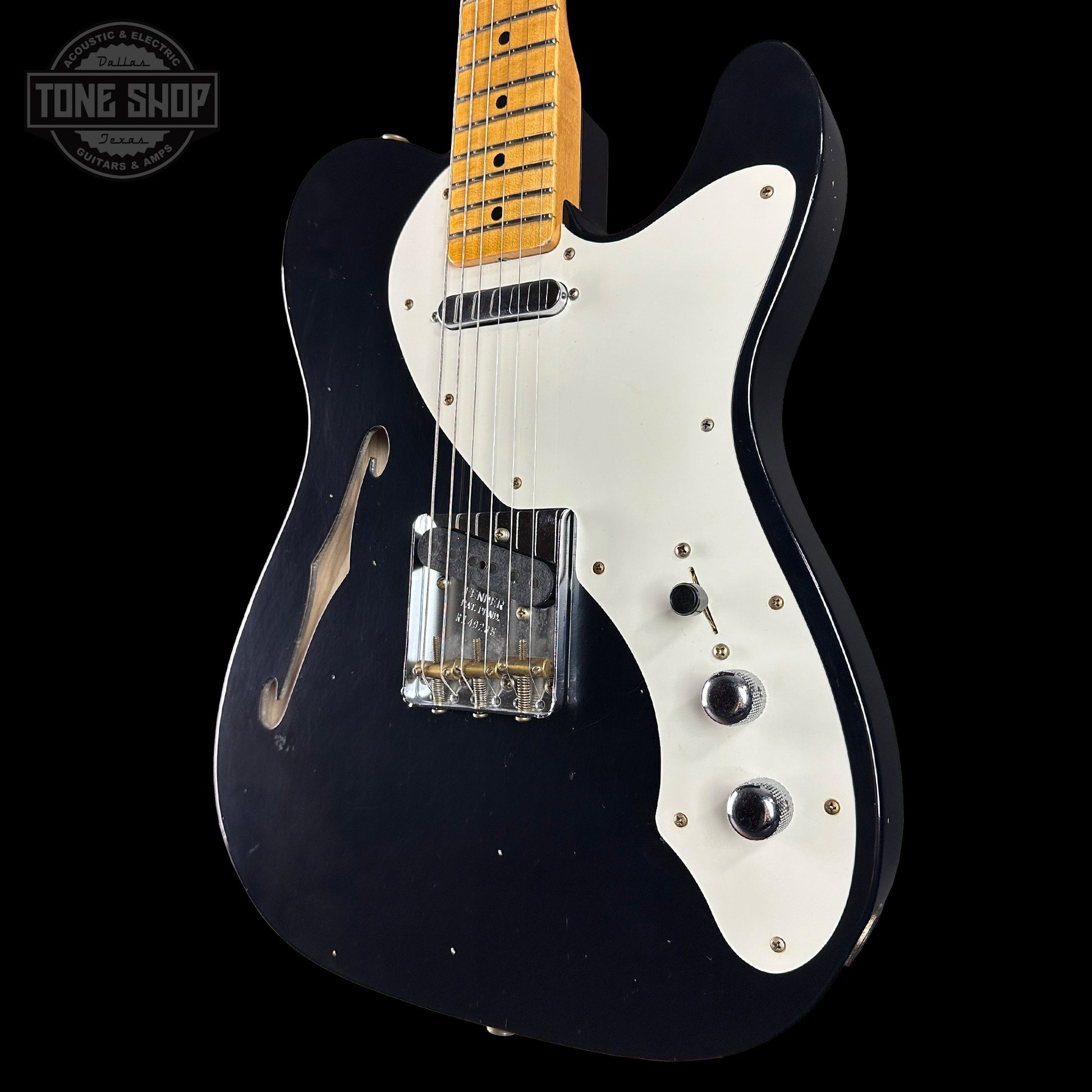 Black electric guitar with white pickguard on a black background, featuring 'Tone Shop' logo.