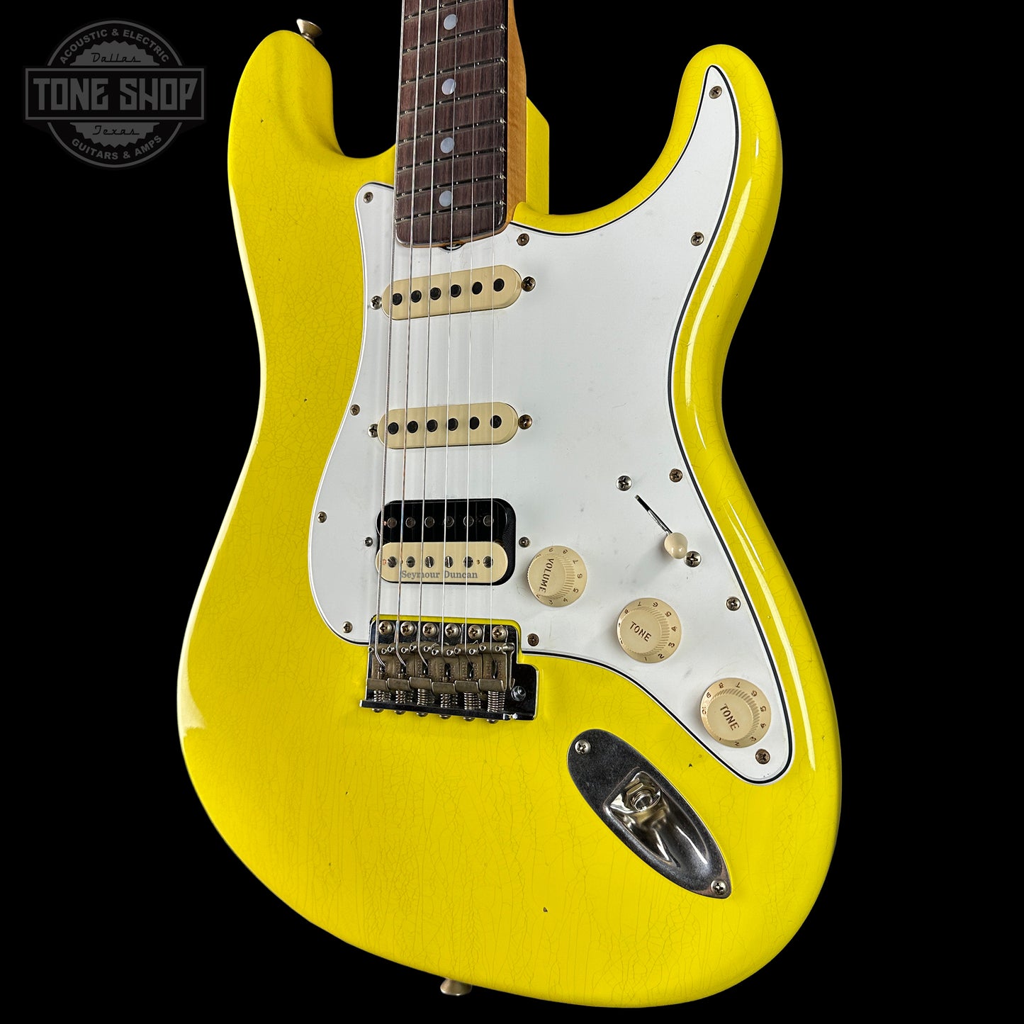 Yellow electric guitar with a white pickguard on a black background, featuring the Tone Shop logo.