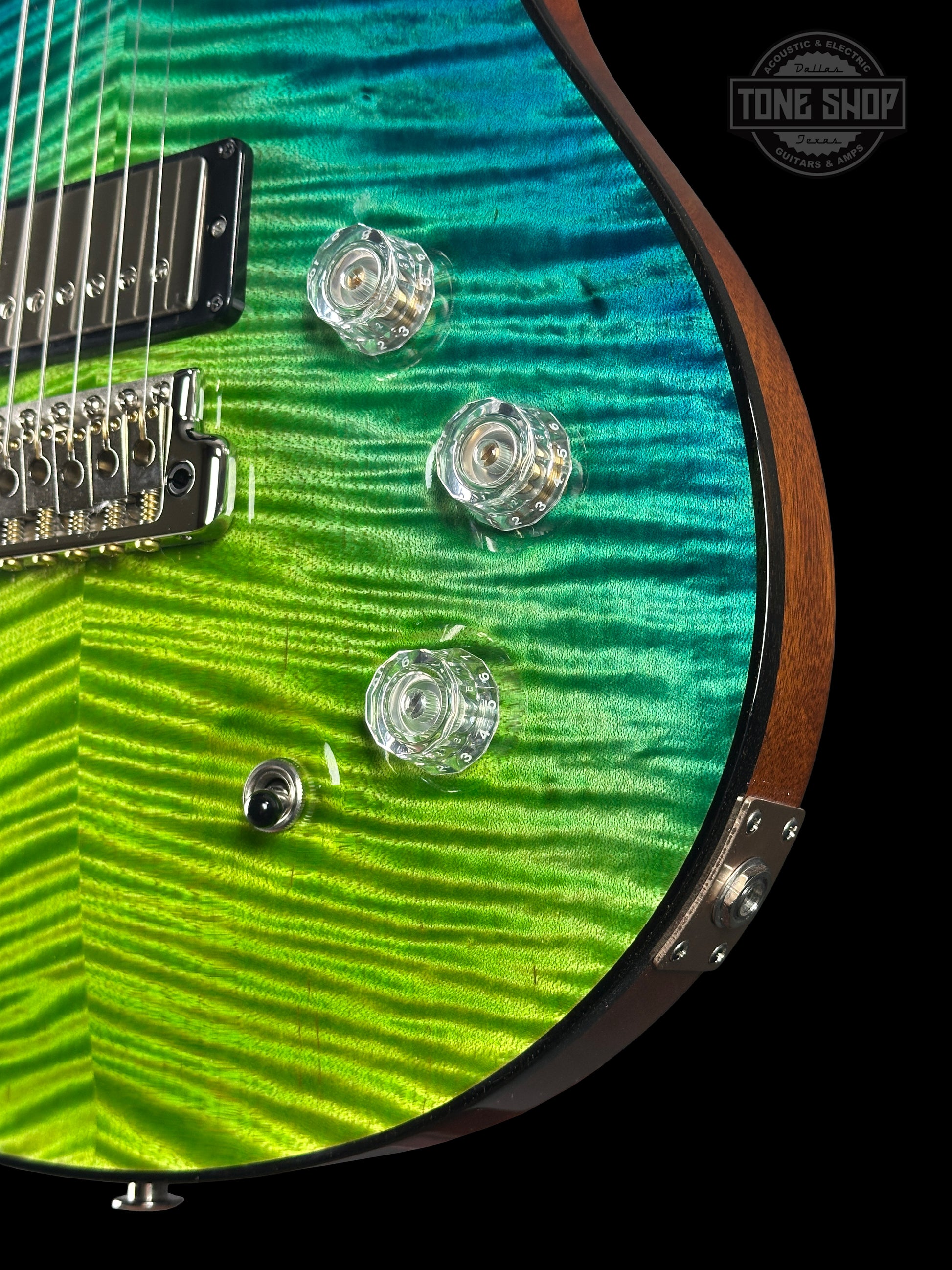 Close-up of a guitar with a green and blue pattern, brand logo visible.