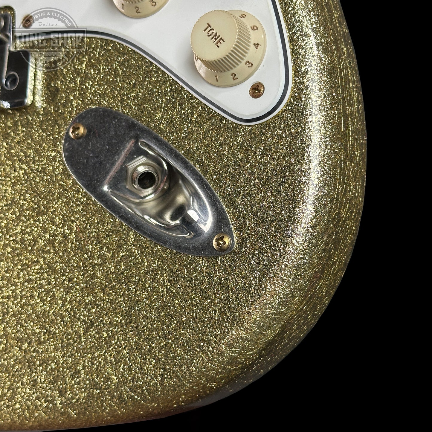 Close-up of a gold glittery guitar with control knobs on a black background